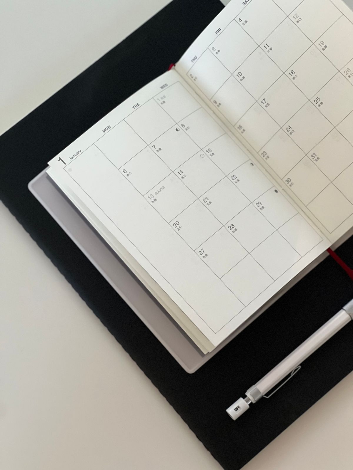 An open planner beside a pen and tablet.