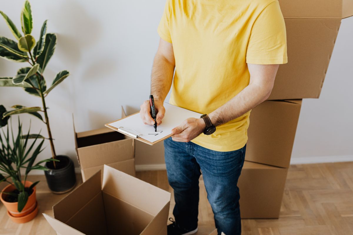 A person recording notes beside cardboard moving boxes.