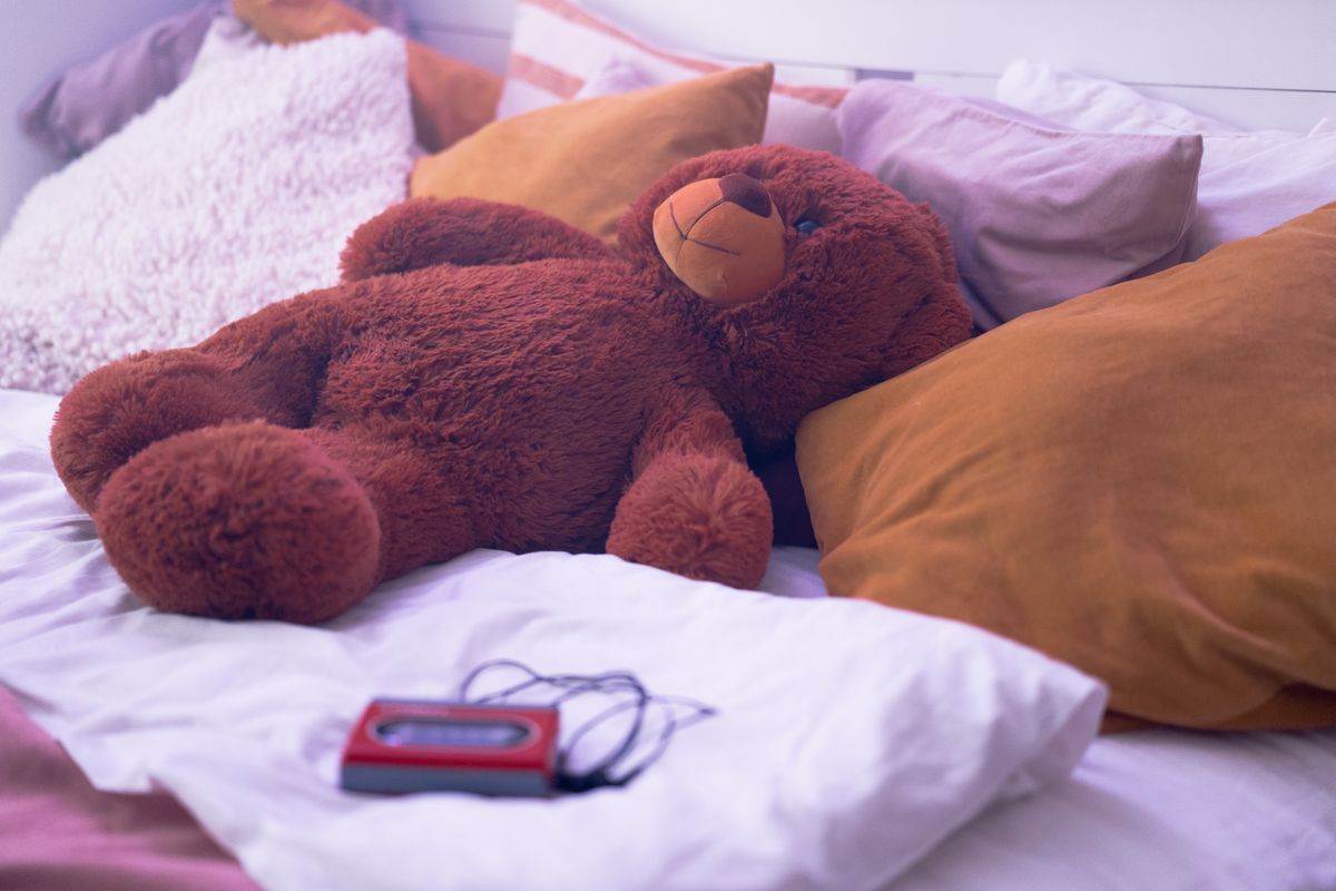 A teddy bear resting on a bed among pillows.