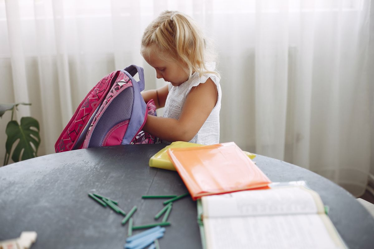 A child looking inside a backpack at a table.
