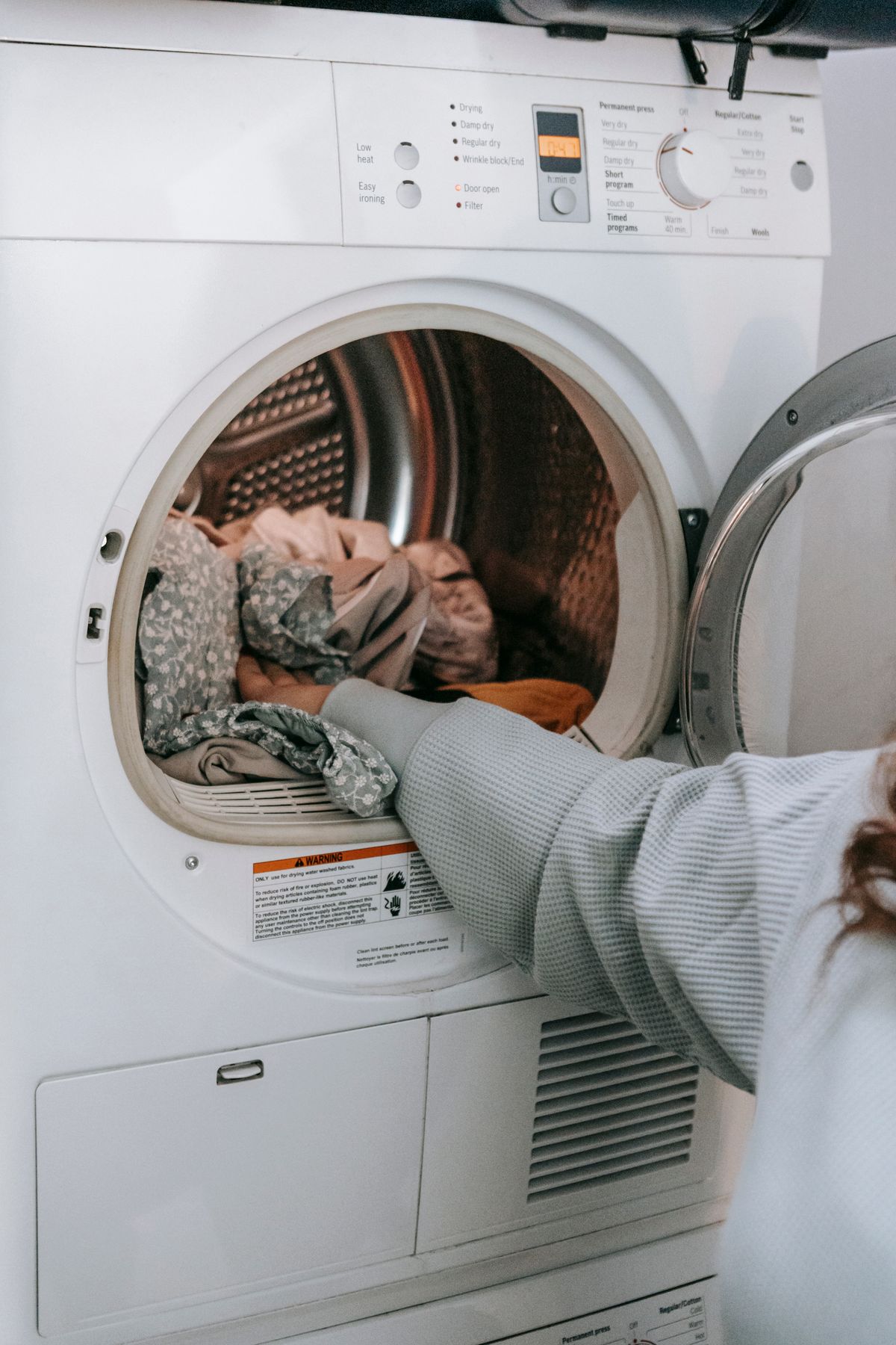 Hands loading clothes into a washing machine.