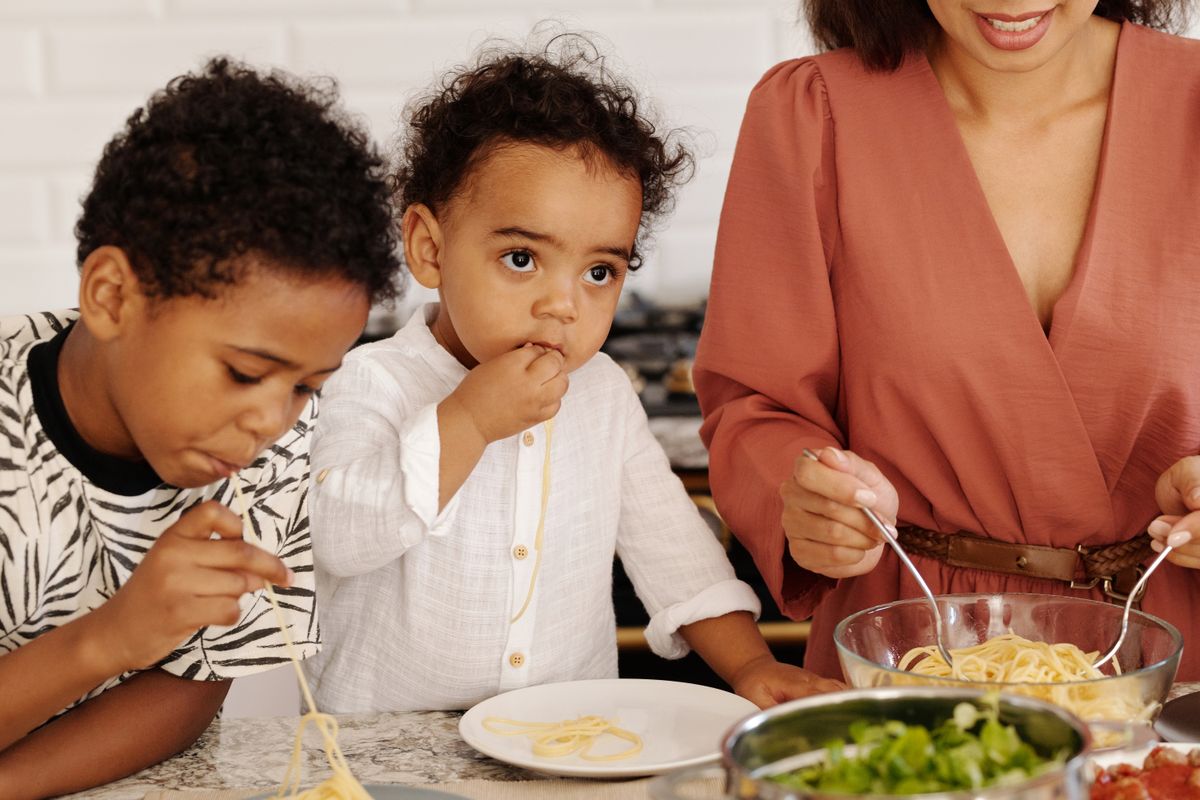 A woman and children eating pasta together at home.
