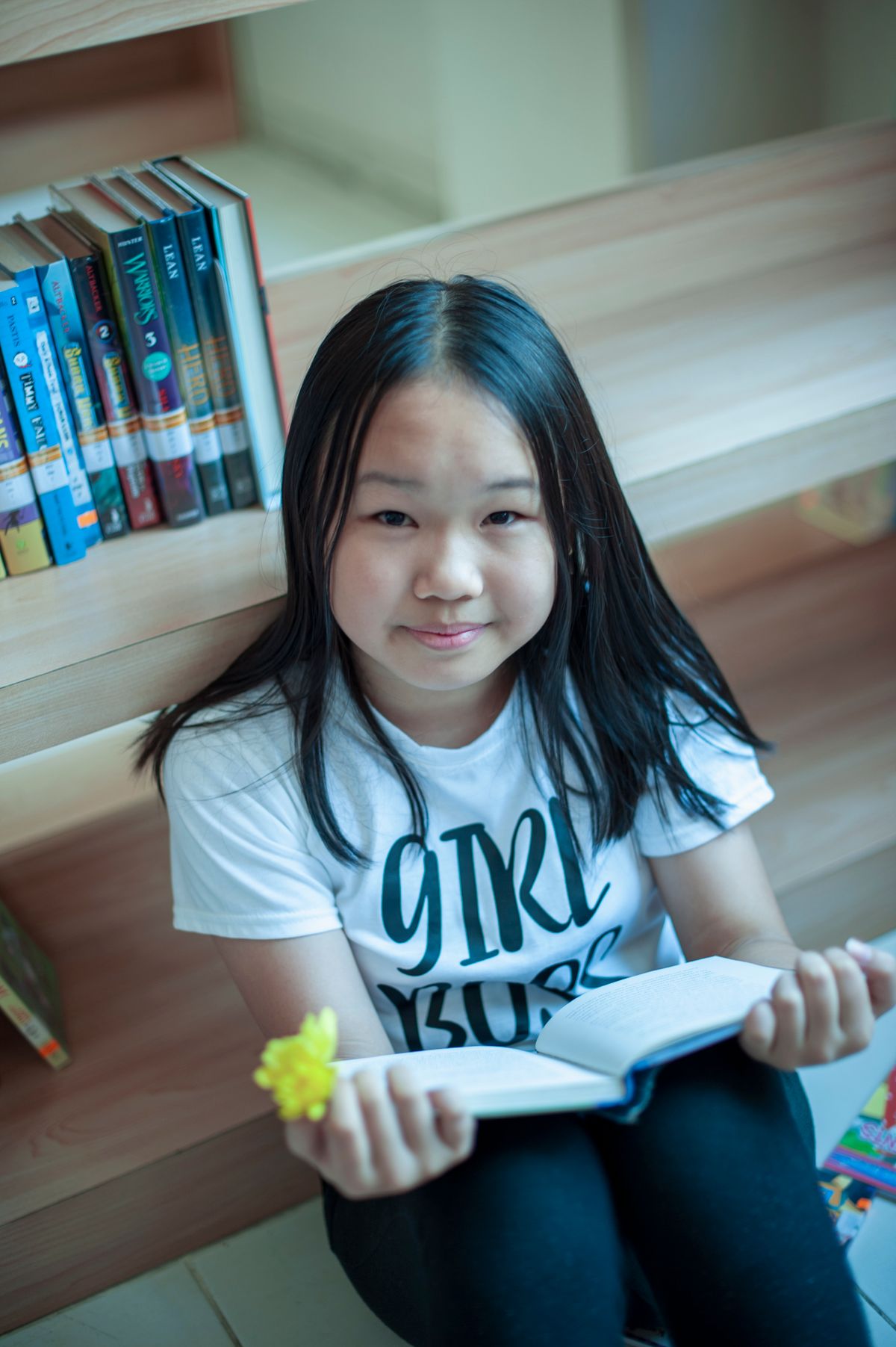 A child reading an open book beside library shelves.