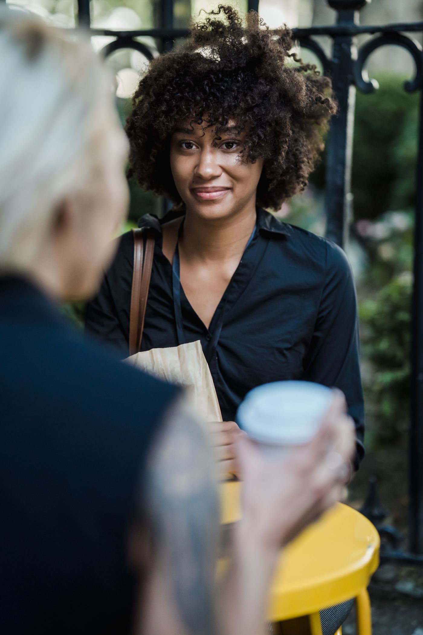 Two women talking with coffee beside an outdoor fence