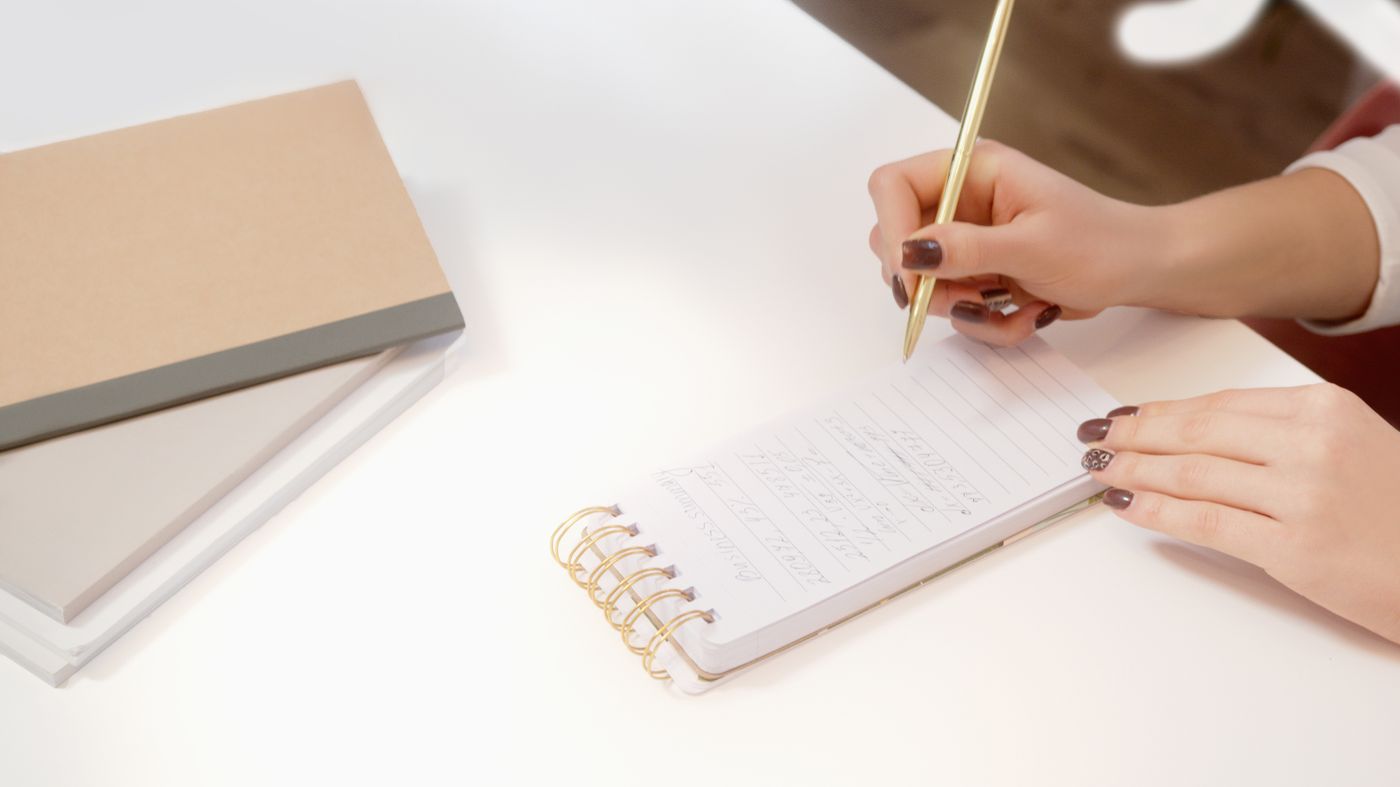 A hand writing notes in a spiral notebook