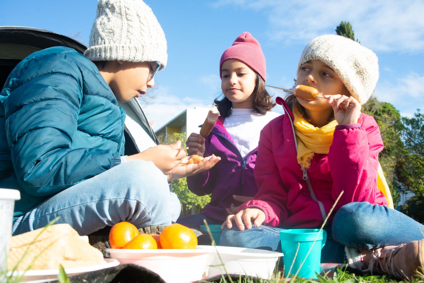 Children sharing food on an outdoor picnic blanket