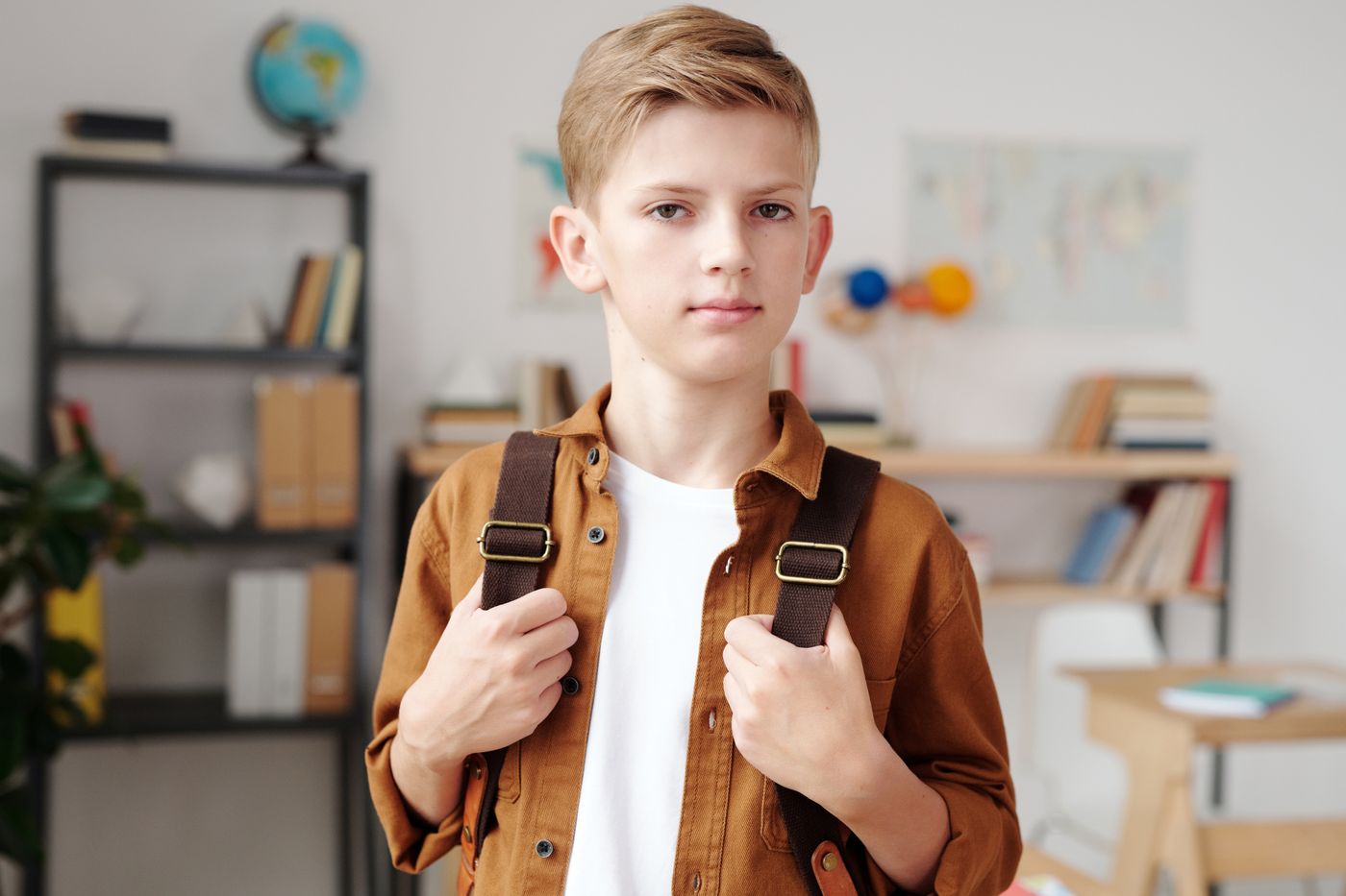 A boy holding his backpack in a classroom