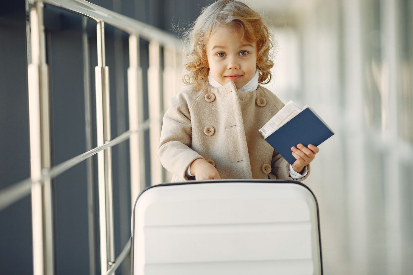 A child holding a passport beside a suitcase