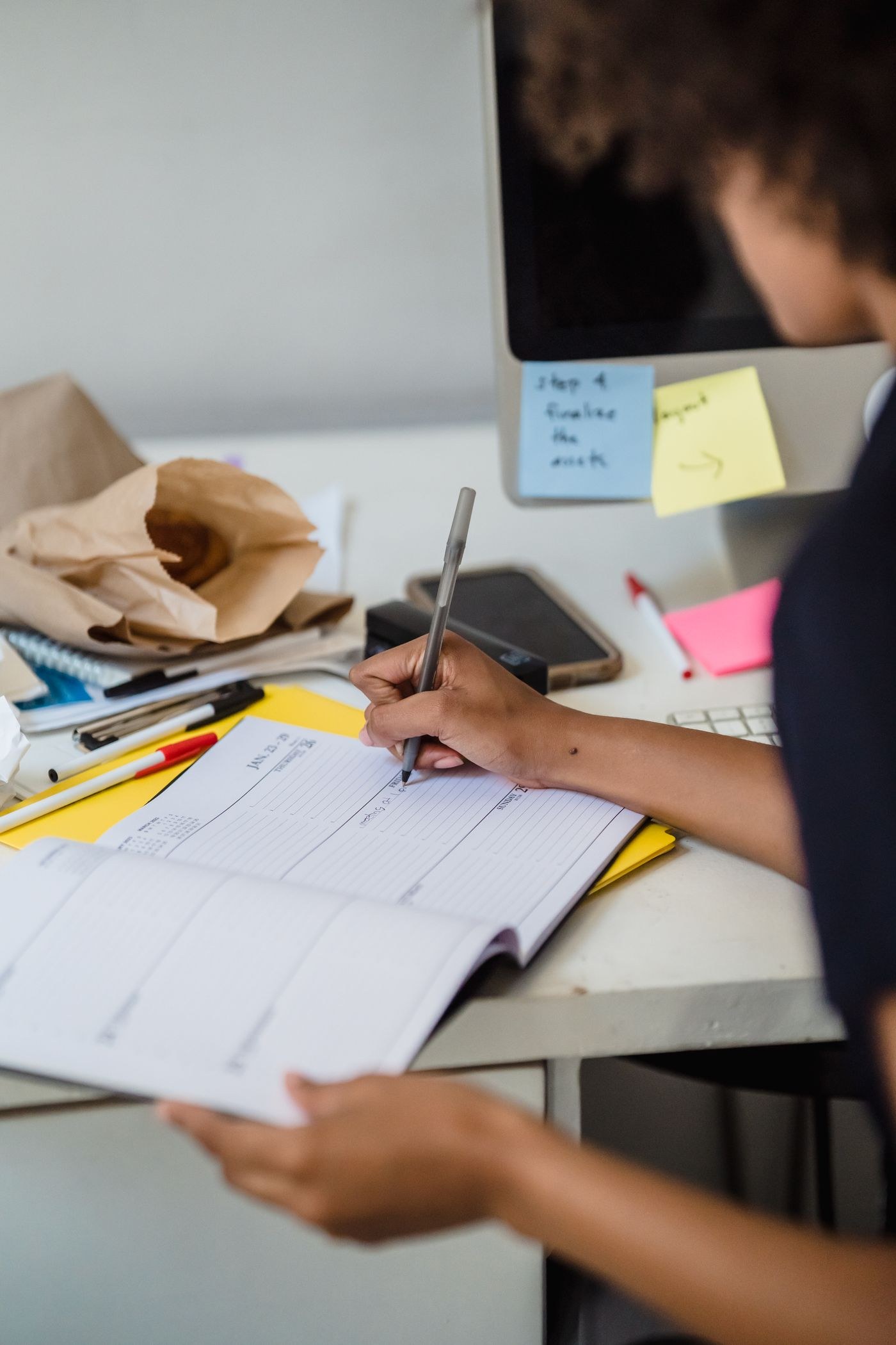 A hand writing in a planner on a desk